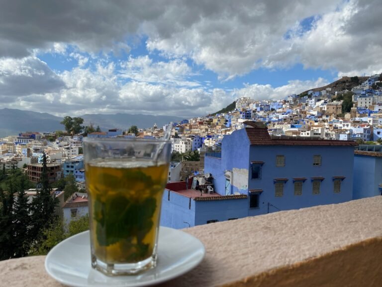 A traditional glass of Moroccan mint tea on a rooftop terrace overlooking the blue buildings of Chefchaouen.