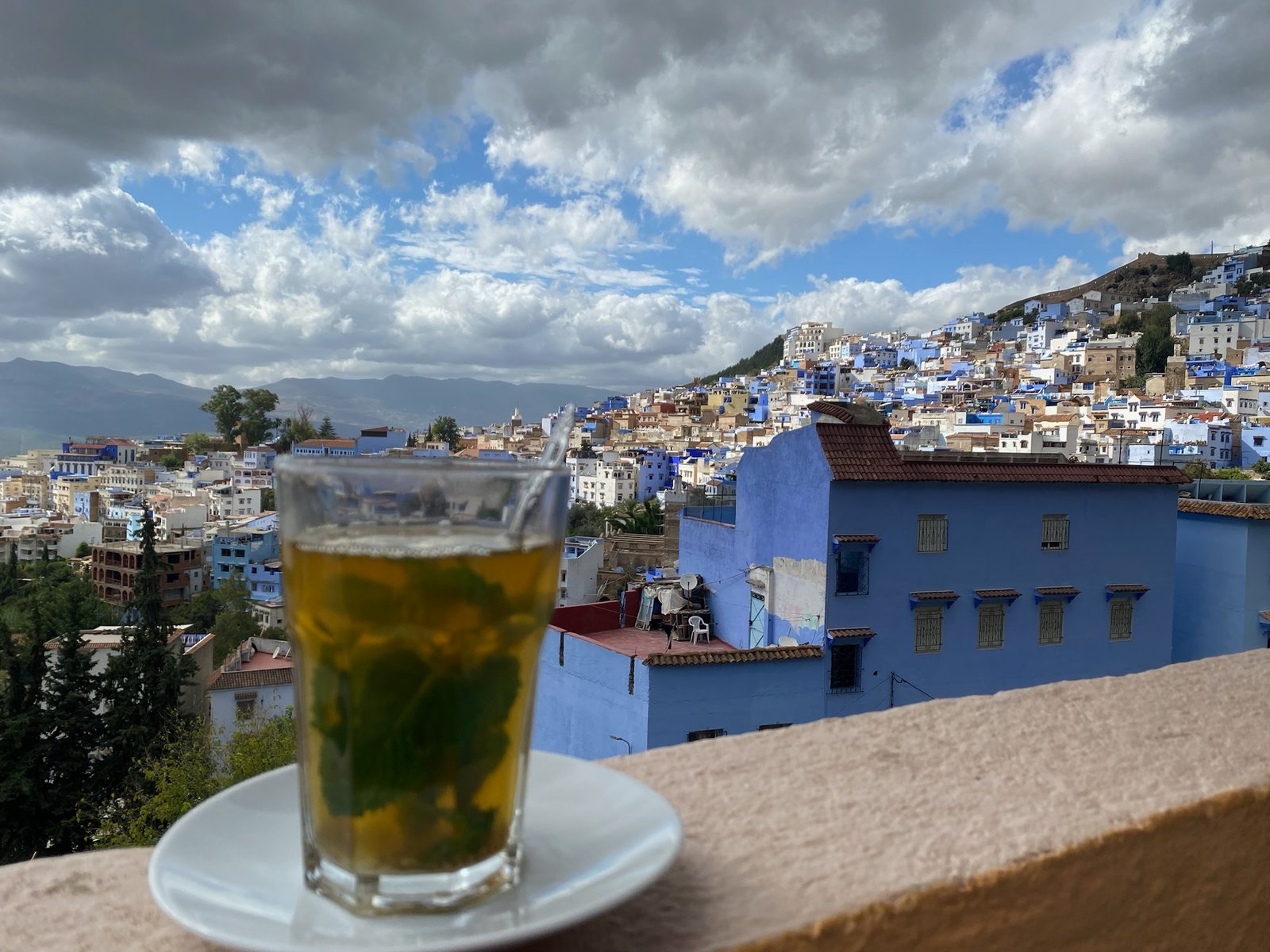 A traditional glass of Moroccan mint tea on a rooftop terrace overlooking the blue buildings of Chefchaouen.