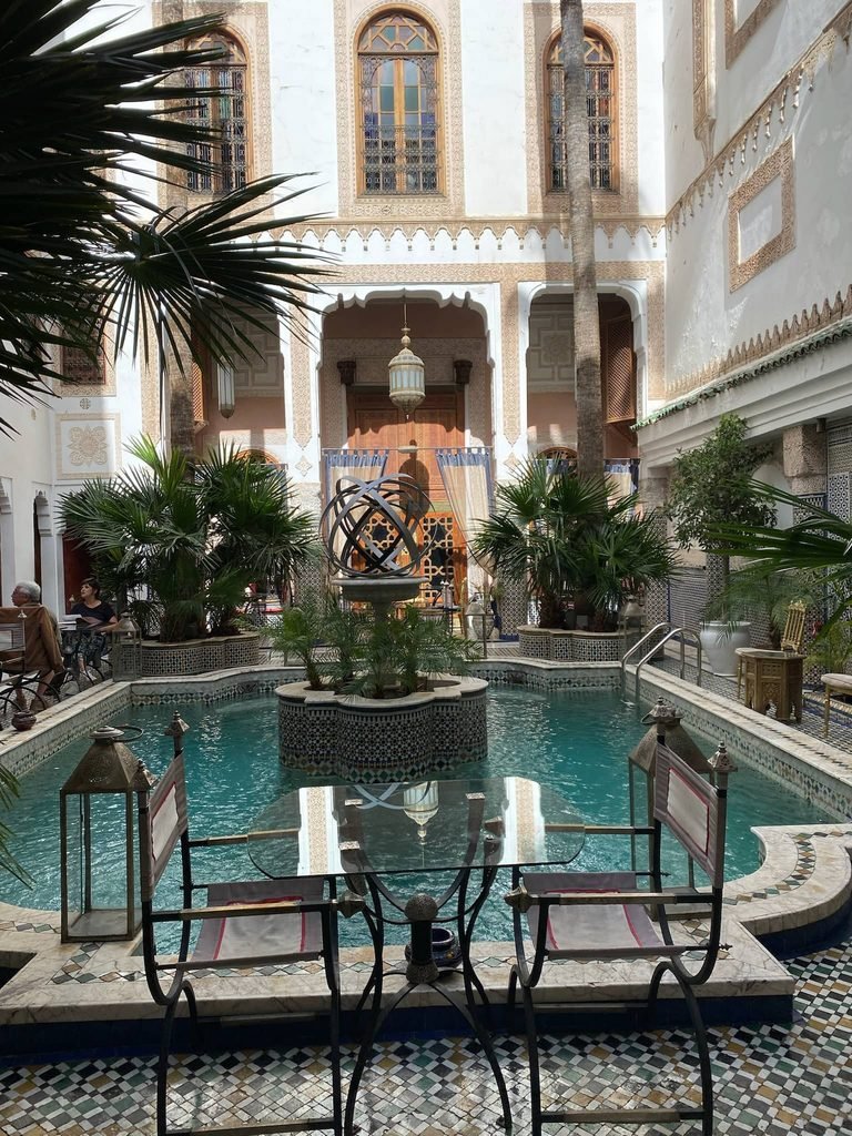 inside a peaceful riad with a table and chairs and water behind