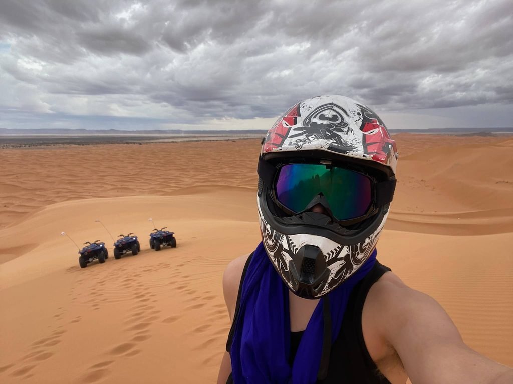 teenager in the sahara with three quad bikes in the distance
