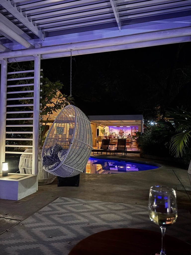 glass of wine in foreground, pool in background at night